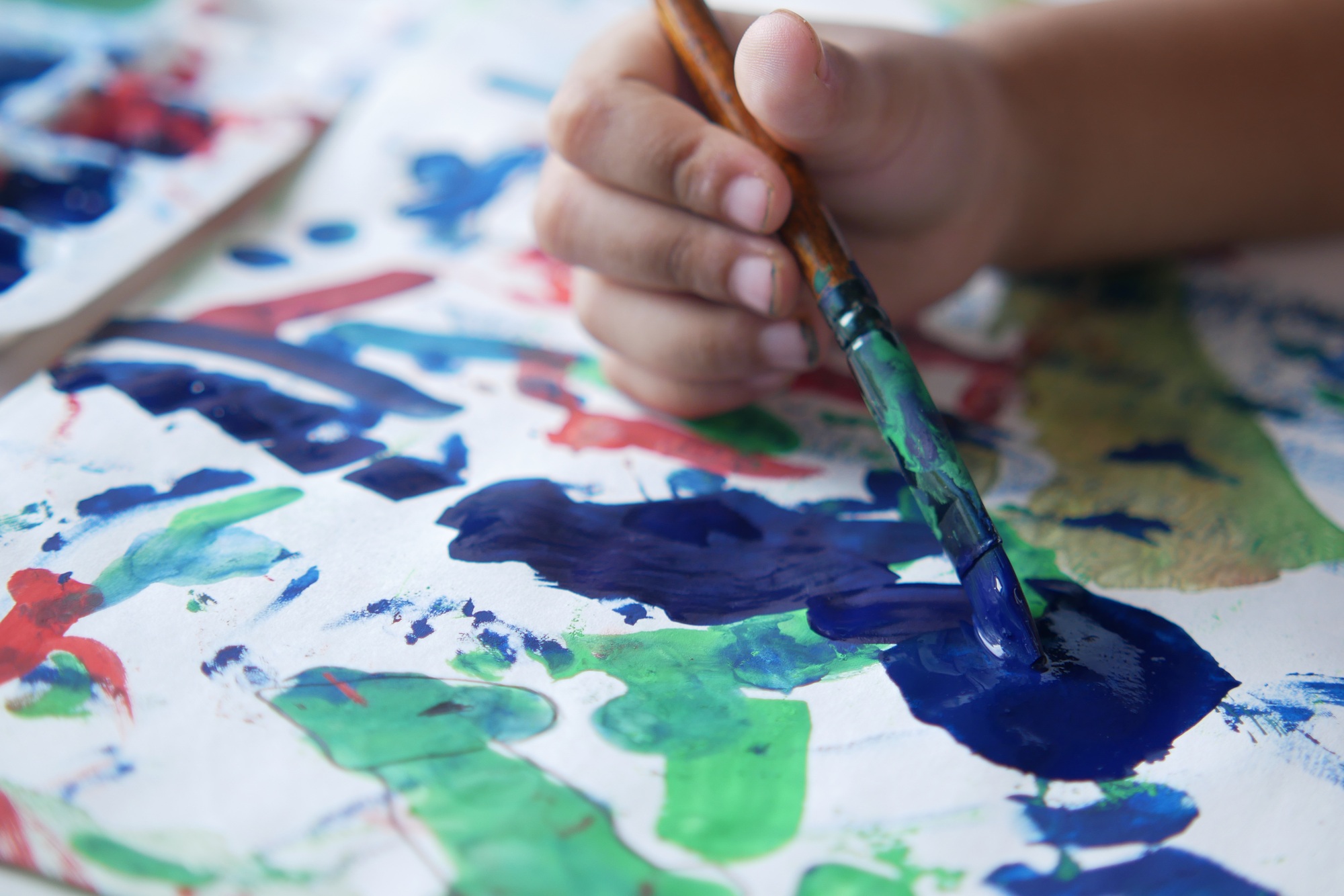 child hand drawing with art brush on a paper